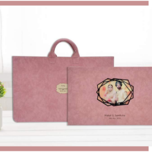 Luxury custom photo album with a blush fabric cover and geometric picture window, shown with a matching premium carrying bag.