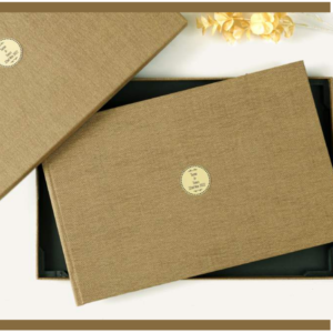 Luxury fabric-covered photo album with a minimalist gold emblem, displayed with a matching presentation box.