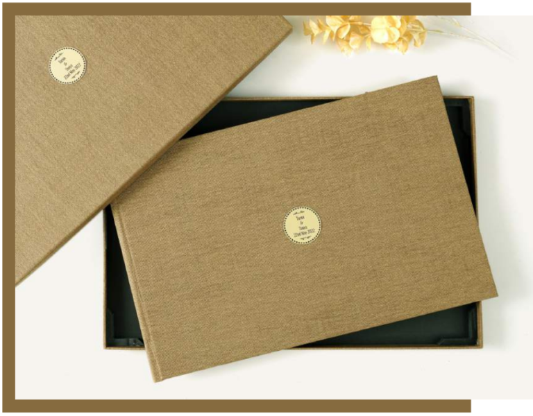 Luxury fabric-covered photo album with a minimalist gold emblem, displayed with a matching presentation box.