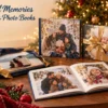 Crafted Memories Christmas photobooks arranged on a wooden table beside wrapped gifts, a holiday mug with marshmallows, pine branches, and a glowing Christmas tree in the background.